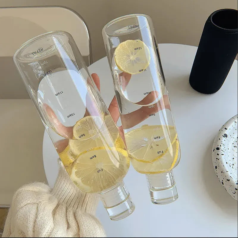 A hand holds a clear insulated water bottle with a time scale and slices of lemon inside.