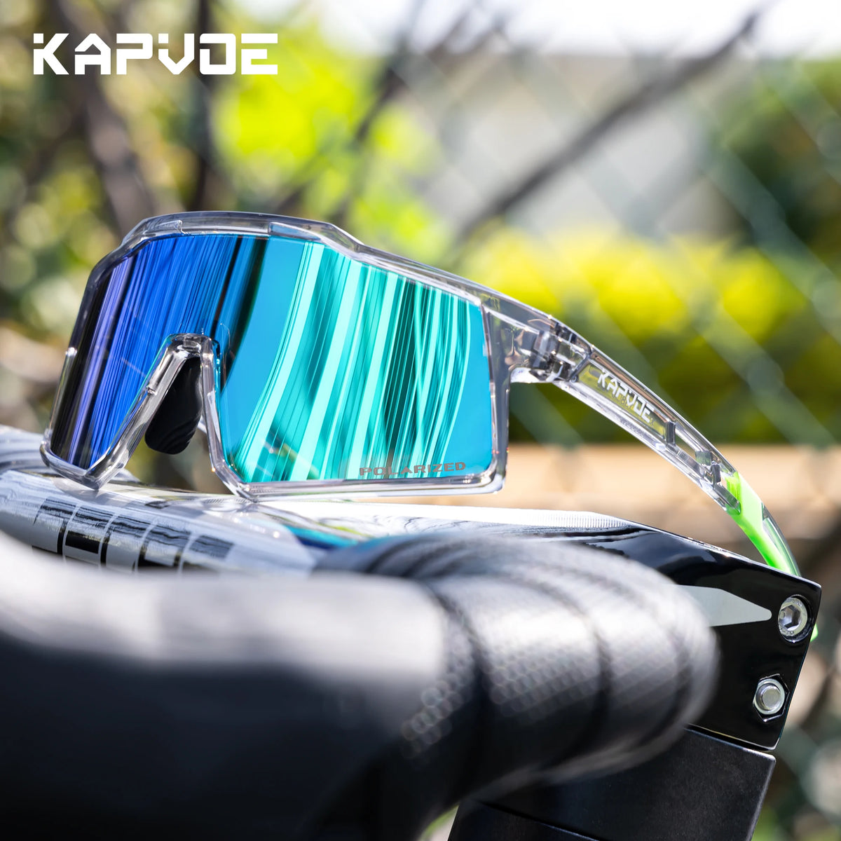 A pair of blue polarized sports sunglasses with a clear frame resting on a black bicycle handlebar.