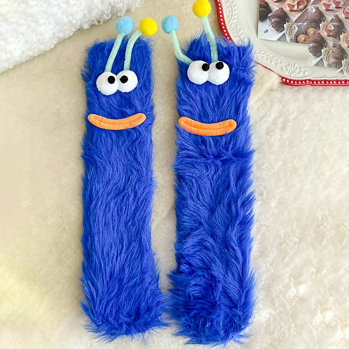 Pair of blue fuzzy plush caterpillar floor socks with yellow antennae and orange mouths