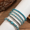 Une pile de cinq bracelets en perles turquoise bohèmes portés au poignet sur fond blanc.