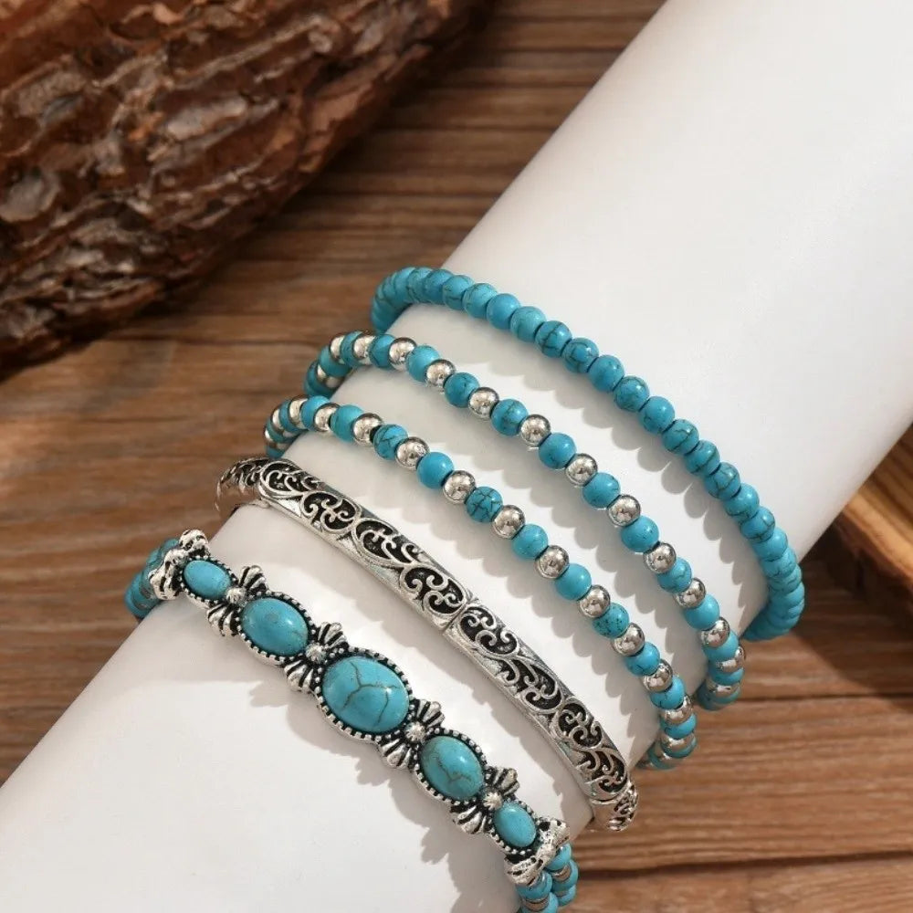 Une pile de cinq bracelets en perles turquoise bohèmes portés au poignet sur fond blanc.