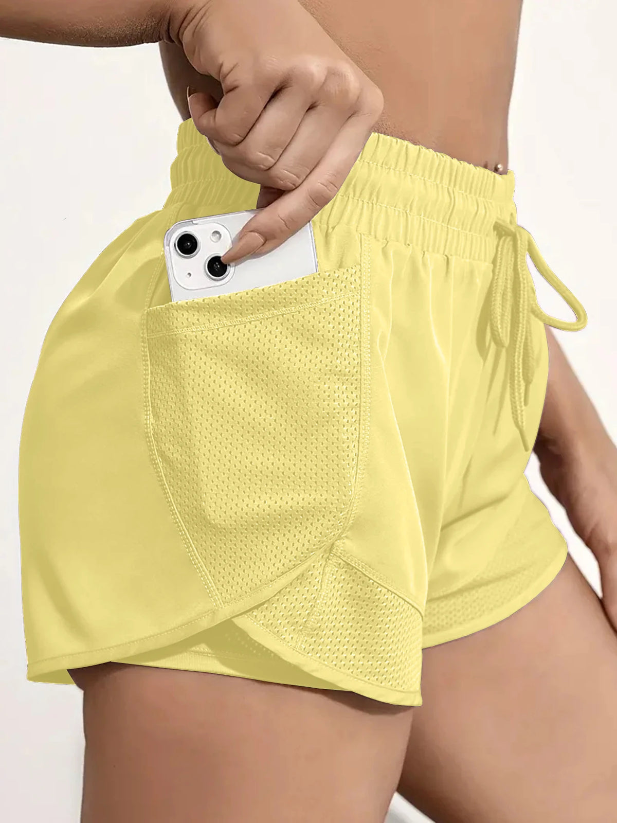 A hand is shown placing a white smartphone into the mesh pocket of a yellow athletic short.