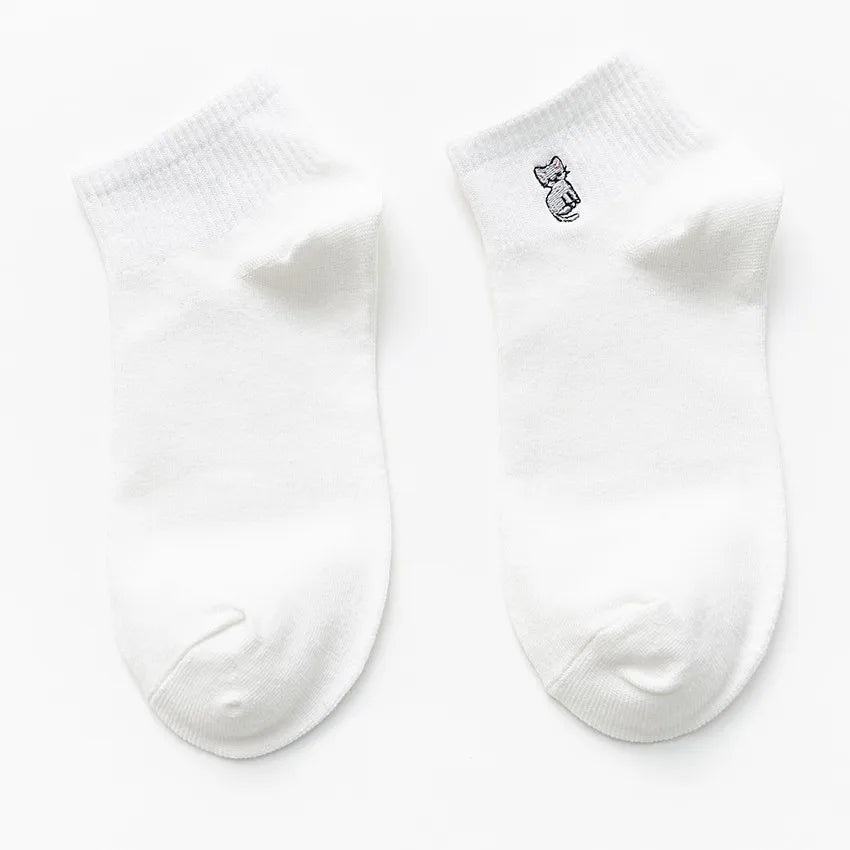 A pair of white cotton socks with a small embroidered cat design on the toe.