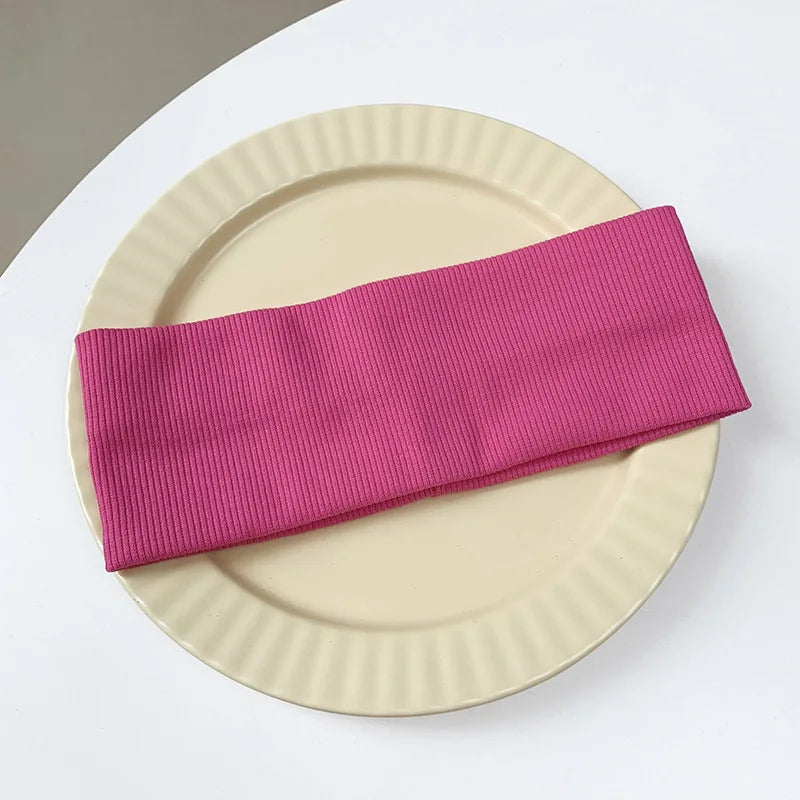 A pink ribbed elastic hairband is placed on a light beige plate.