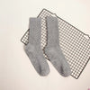 Gray mid-calf yoga and pilates socks laid on a black grid mat.