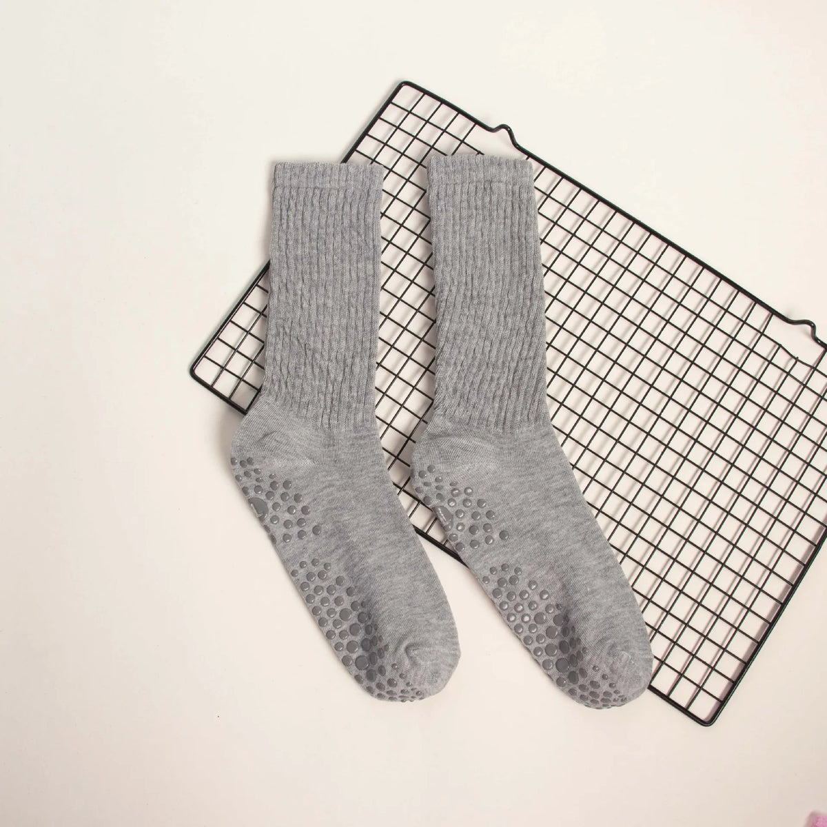 Gray mid-calf yoga and pilates socks laid on a black grid mat.