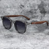 A pair of trendy sunglasses with dark lenses and a brown wood grain frame resting on a gray textured surface.
