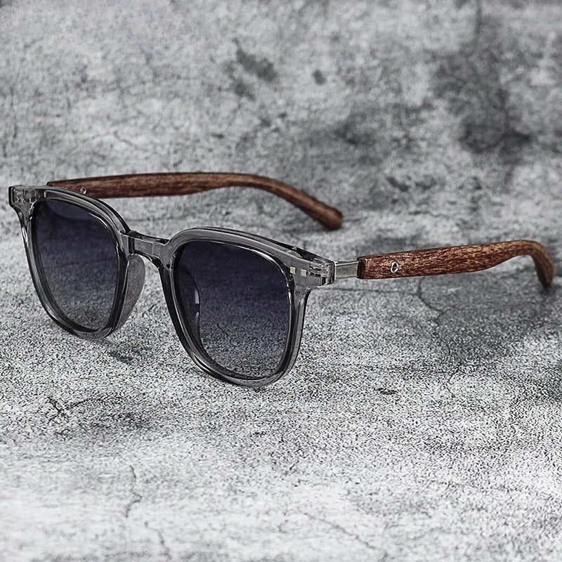 A pair of trendy sunglasses with dark lenses and a brown wood grain frame resting on a gray textured surface.