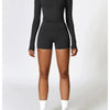 A woman wearing a black long sleeve yoga and fitness t-shirt and matching shorts, standing full length.