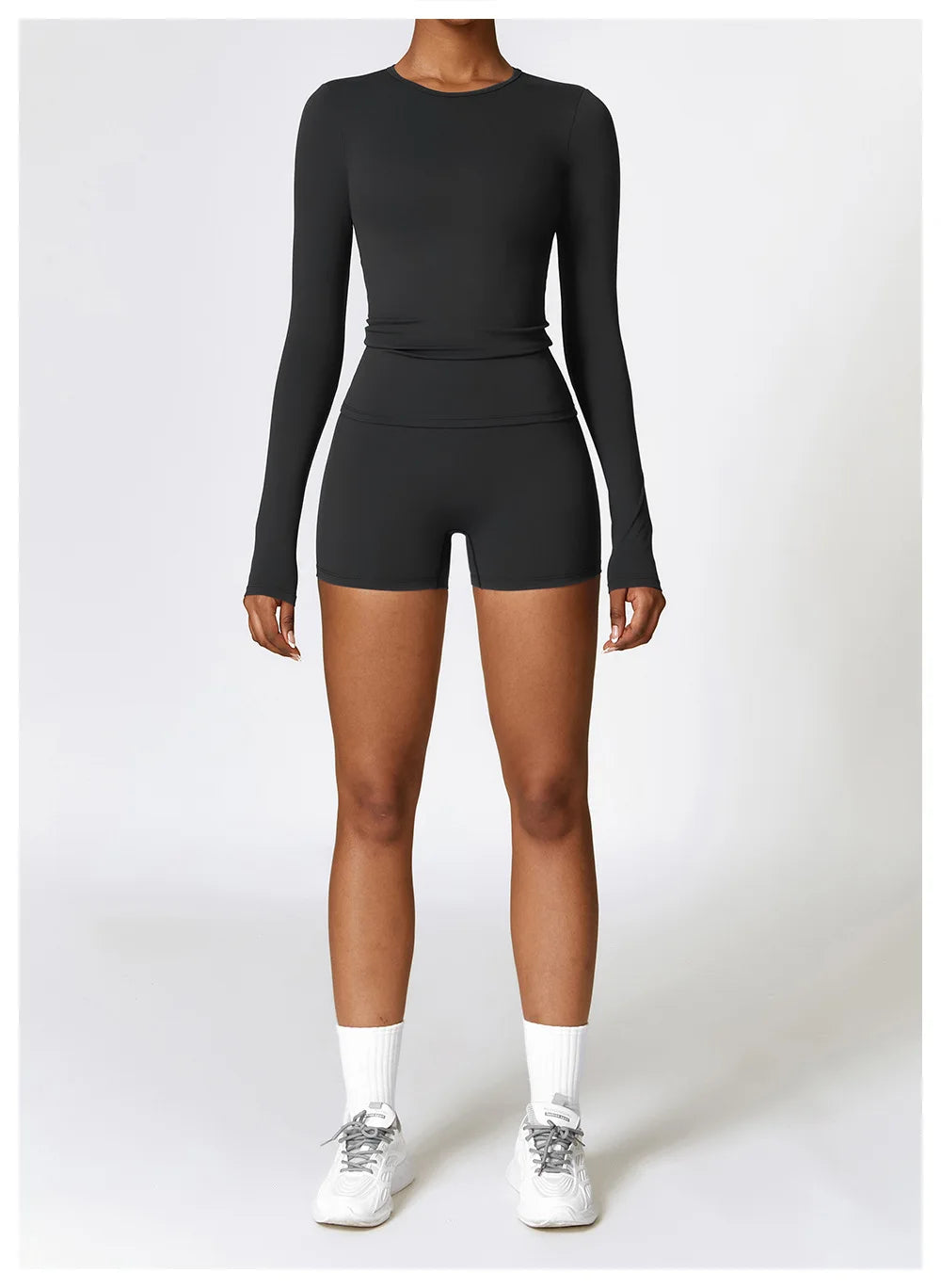 A woman wearing a black long sleeve yoga and fitness t-shirt and matching shorts, standing full length.