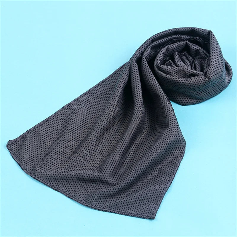 A dark gray microfiber cooling towel is rolled up on a light blue background.