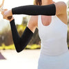 A woman wearing black arm sleeves and a white top is holding a cycling implement outdoors.
