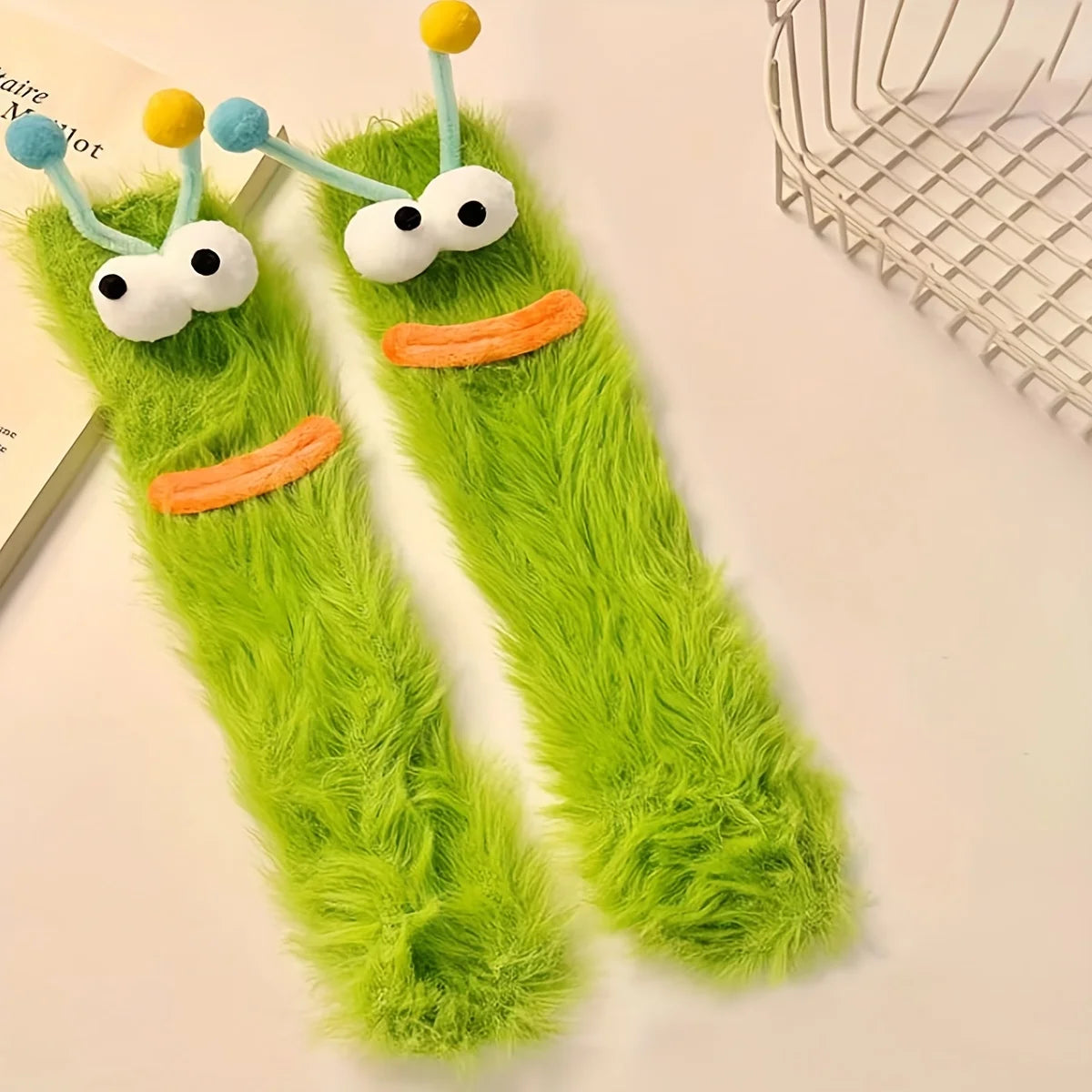 Pair of funny plush caterpillar floor socks with green fuzzy texture and yellow and blue accents
