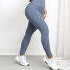 A woman wearing high-waisted gray sports leggings and white sneakers standing indoors.