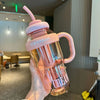 A hand holds a pink glass sports water bottle with a pink silicone straw and a pink silicone lid.