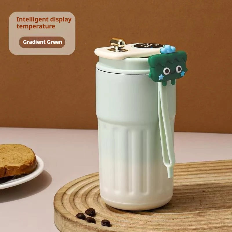 A white thermo mug with a gradient green display and a dark green lid is shown on a wooden surface.