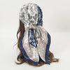 Elegant satin square scarf featuring intricate paisley patterns in silver, white, and navy blue.