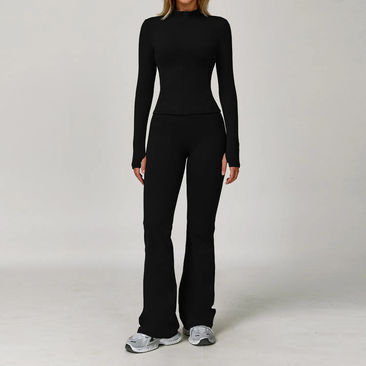 A woman wearing a black 3-piece yoga sports set consisting of a long-sleeved top and matching pants.