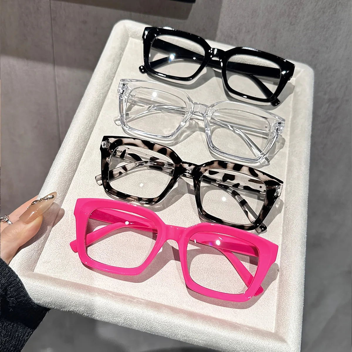 A display of various square anti-blue light eyewear frames in black, clear, and pink colors.