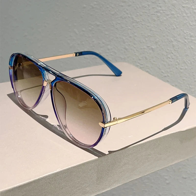 Vintage pilot gradient sunglasses with blue frames and gold accents resting on a white surface.