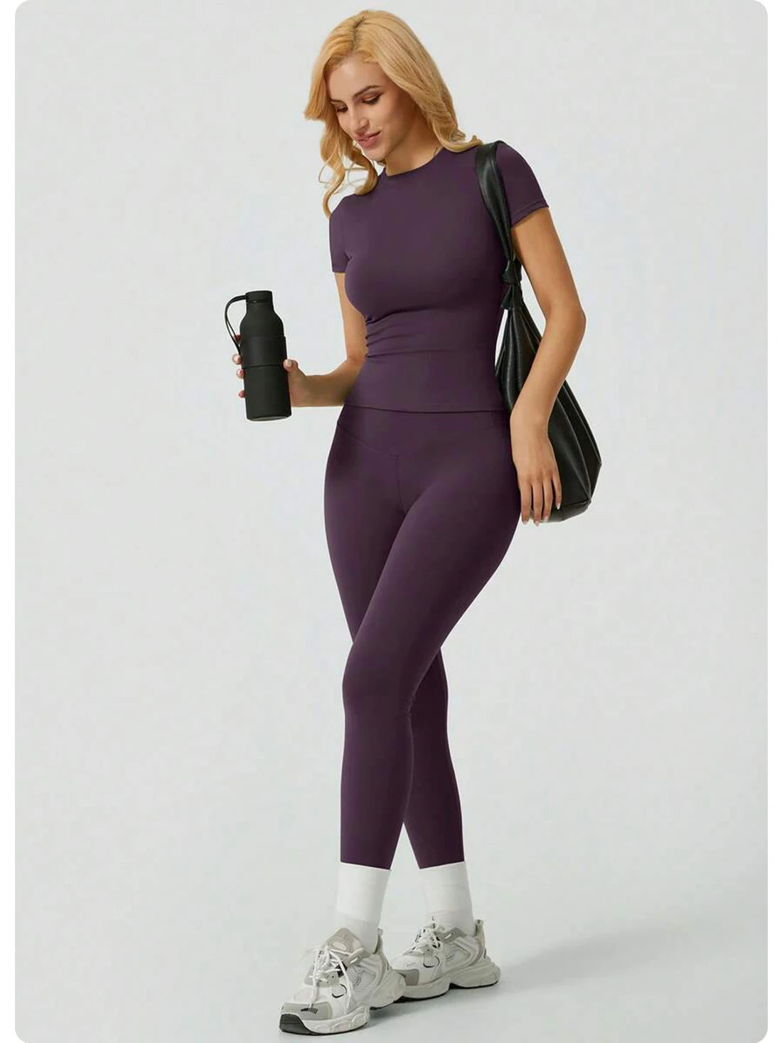 Eine Frau modelliert ein lila Zweiteil-Yoga-Set mit hohen Bund-Leggings und einem kurzärmeligen Oberteil.