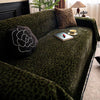 A dark green plush sofa cover blanket with a leopard print pattern, featuring decorative pillows and a small tray.