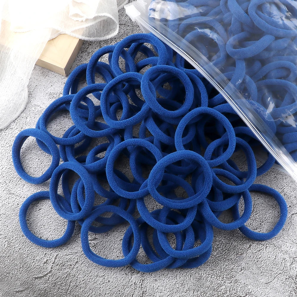 A pile of blue elastic hair bands and a clear plastic sheet are shown on a gray surface.