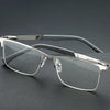 A pair of silver-framed reading glasses with dark gray patterned temples and clear lenses resting on a dark surface.