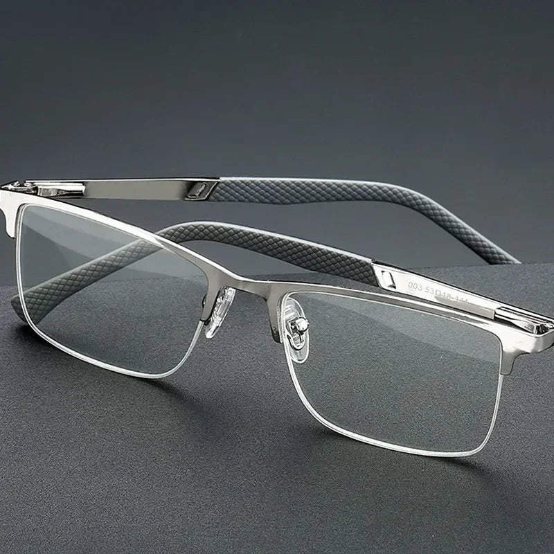 A pair of silver-framed reading glasses with dark gray patterned temples and clear lenses resting on a dark surface.