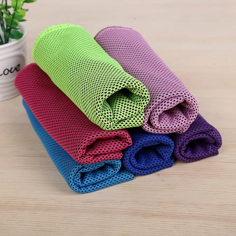 A stack of colorful microfiber cooling towels in shades of green, pink, purple, and blue on a wooden surface.