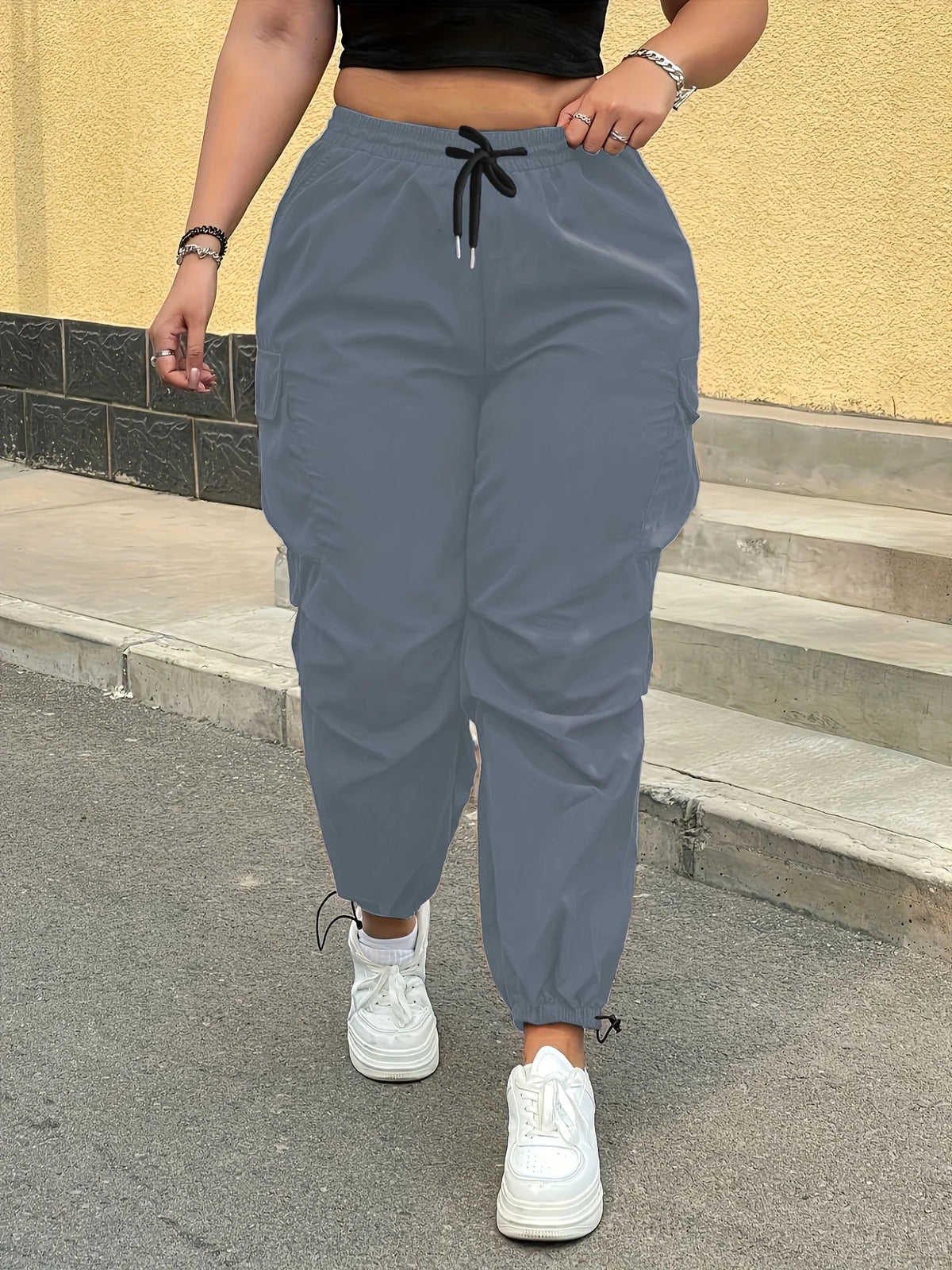 A person wearing gray high-waist drawstring cargo joggers standing outdoors on steps.