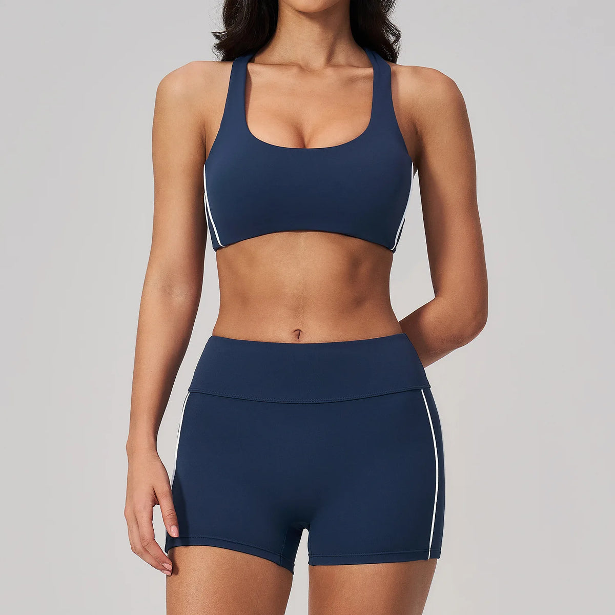 A woman wearing a navy blue two-piece yoga and sports tracksuit set consisting of a cropped top and matching shorts.