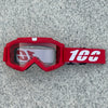 A pair of red heavy-duty motorcycle and ATV goggles with a white logo and black strap resting on a gray surface.