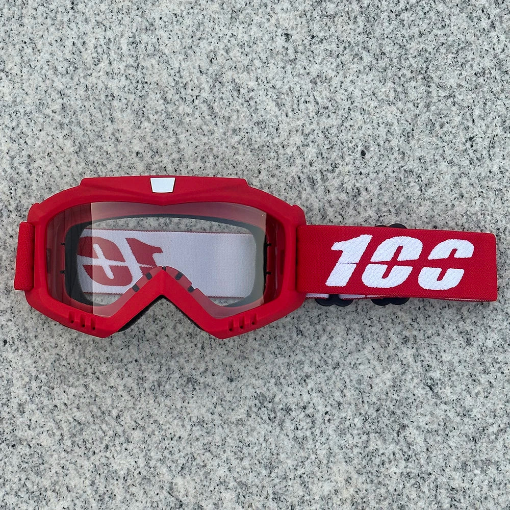 A pair of red heavy-duty motorcycle and ATV goggles with a white logo and black strap resting on a gray surface.