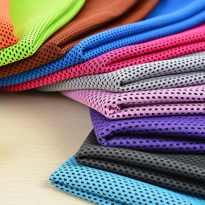 A stack of colorful microfiber cooling towels in various shades of pink, purple, blue, and black on a wooden surface.