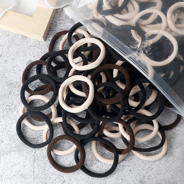 A pile of 50 mixed color elastic hair bands in black, brown, and beige are displayed on a light surface.
