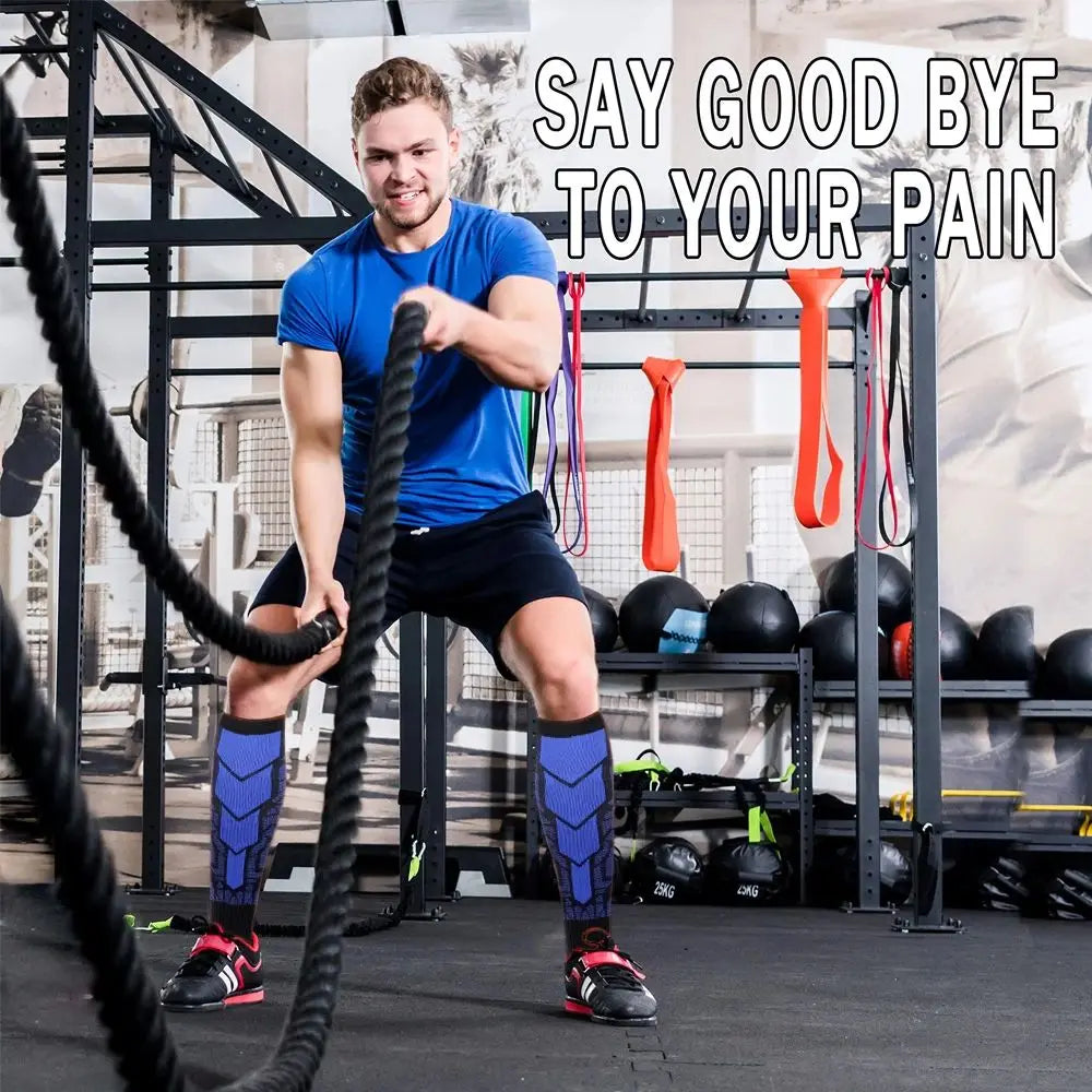 A muscular man in a blue shirt and black shorts performs a workout using a black cable machine, with compression socks visibl