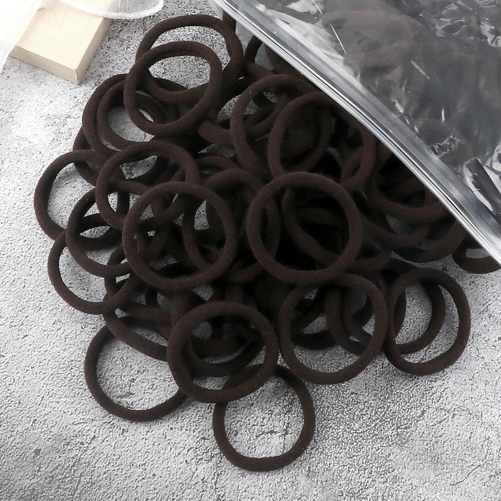A pile of dark brown elastic hair bands is shown next to a clear plastic sheet.