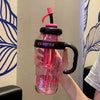 A hand holds a pink and clear iced bottle with a black lid and sleeve against a light background.