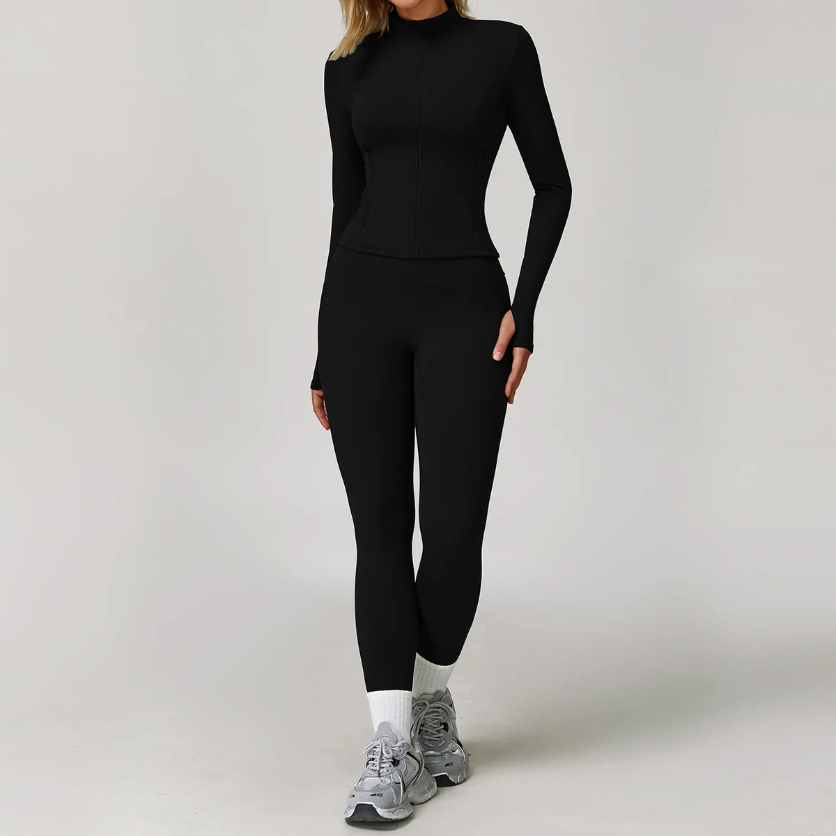 A woman wearing a black long-sleeved top and leggings with white socks and gray athletic shoes.