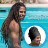 A man with dreadlocks is smiling while wearing a black unisex extra large swimming cap in a bright blue pool.