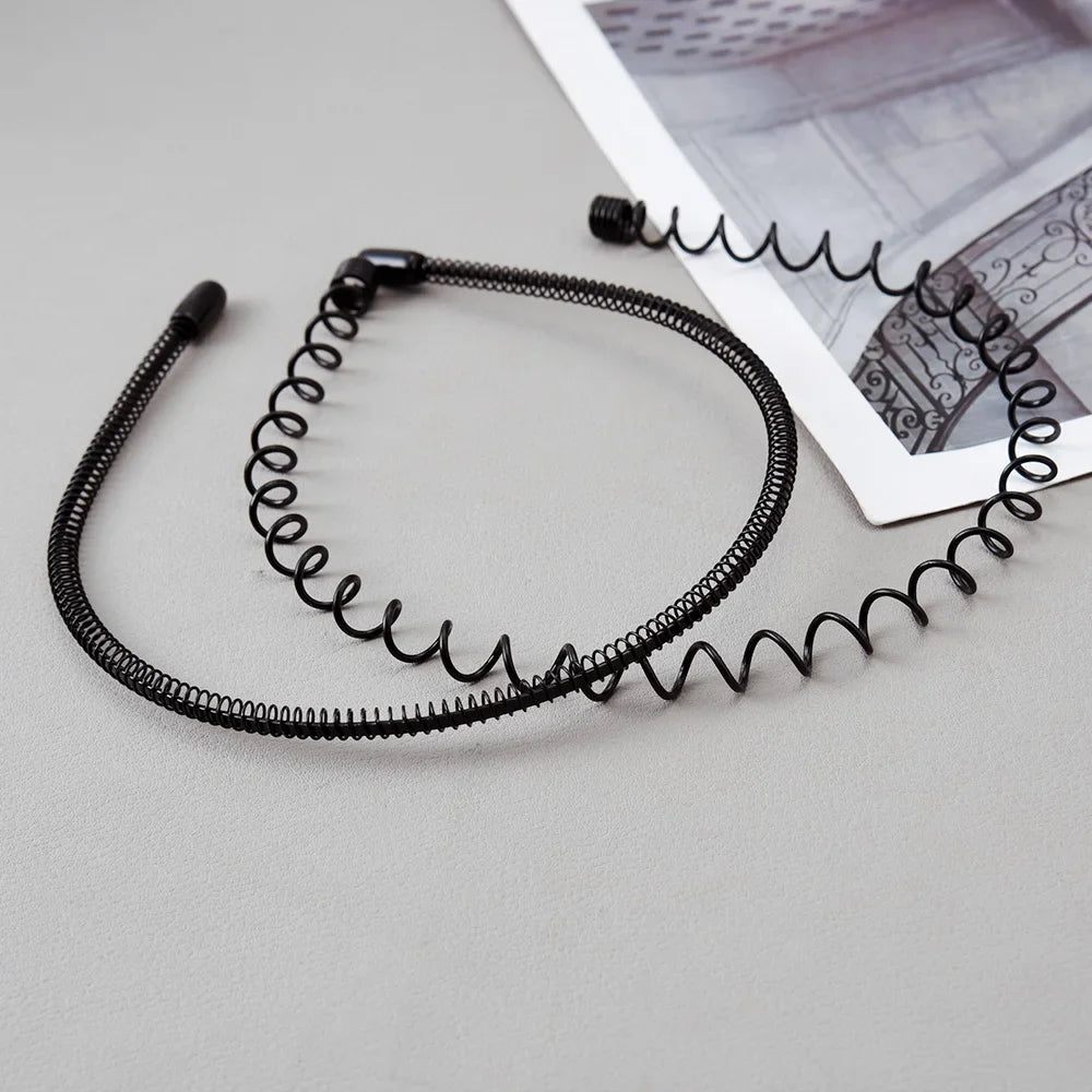 Black coiled metal hair bands laid on a light gray surface next to a piece of paper.