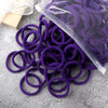 A pile of purple elastic hair bands, some in a clear plastic bag, resting on a gray surface.