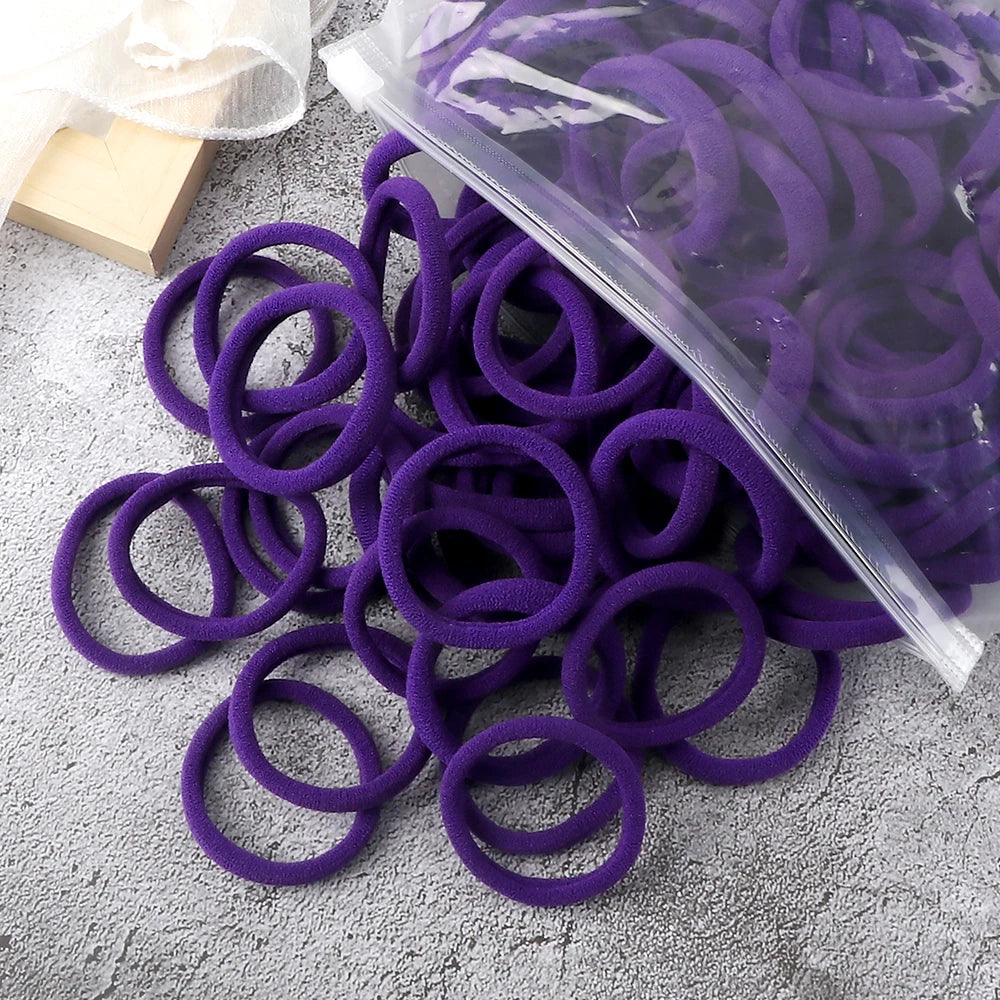 A pile of purple elastic hair bands, some in a clear plastic bag, resting on a gray surface.