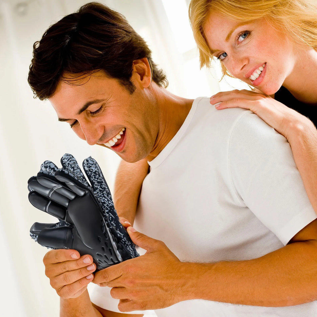 A man is showing a pair of black goalkeeper gloves to a woman in a bright indoor setting.