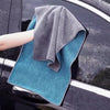 A gray microfiber car cleaning towel is draped over a dark car surface with water droplets visible.