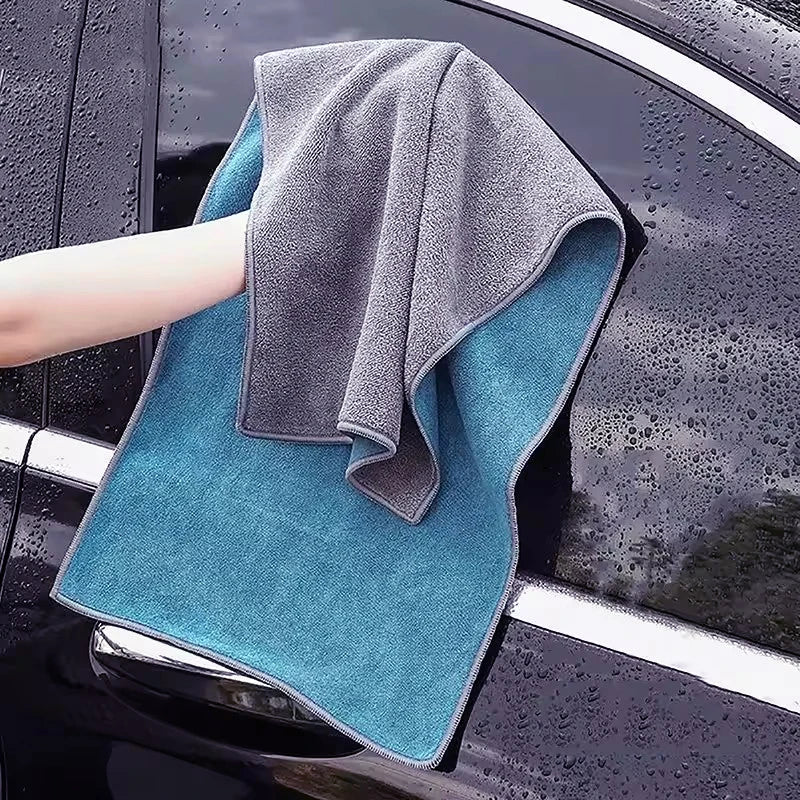 A gray microfiber car cleaning towel is draped over a dark car surface with water droplets visible.
