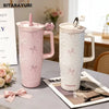 A pink and white insulated thermos mug with floral inlay designs is displayed on a table.