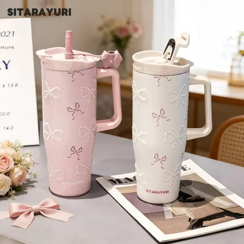 A pink and white insulated thermos mug with floral inlay designs is displayed on a table.