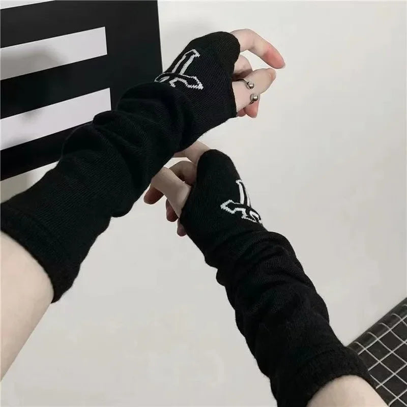 Eine Hand trägt schwarze Fingerless-Armwärmer mit weißen Gothic-Designs vor hellem Hintergrund.